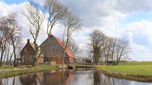 Et traditionelt hollandsk hus med rødt tag, en lille bro over en kanal, og en and svømmer i vandet.
