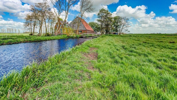En kanal med en træbro, en græsmark og et traditionelt hus med rødt tag.