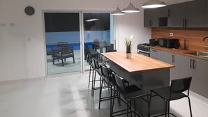 Une cuisine moderne dotée d’un îlot central, de tabourets de bar noirs, de luminaires suspendus et offrant une vue sur un balcon.