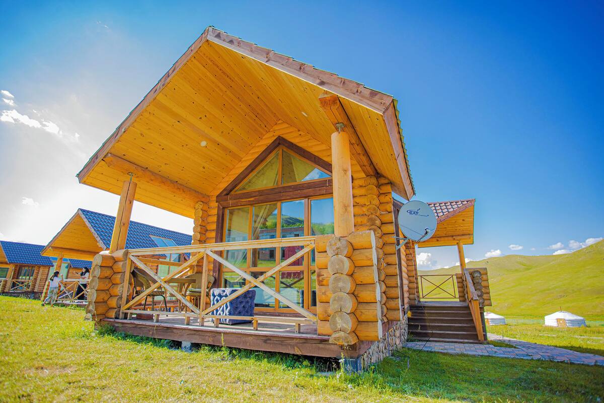 Una cabaña de madera con balcón, ventanas grandes y una antena parabólica.