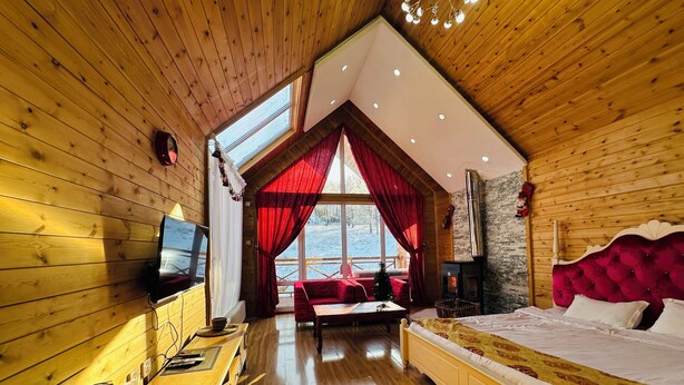 A cozy wooden cabin bedroom with a large bed, a fireplace, a TV, and a view of the snowy landscape. - Bayan Mongolian Resort - Genghis Khan Statue (Erdene)