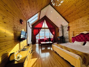 A cozy wooden cabin bedroom with a large bed, a fireplace, a TV, and a view of the snowy landscape. - Bayan Mongolian Resort - Genghis Khan Statue (Erdene)