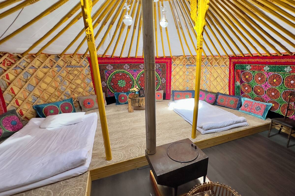 Interior de una yurta tradicional con dos camas, tapices de colores en las paredes y una estructura central de postes de madera.