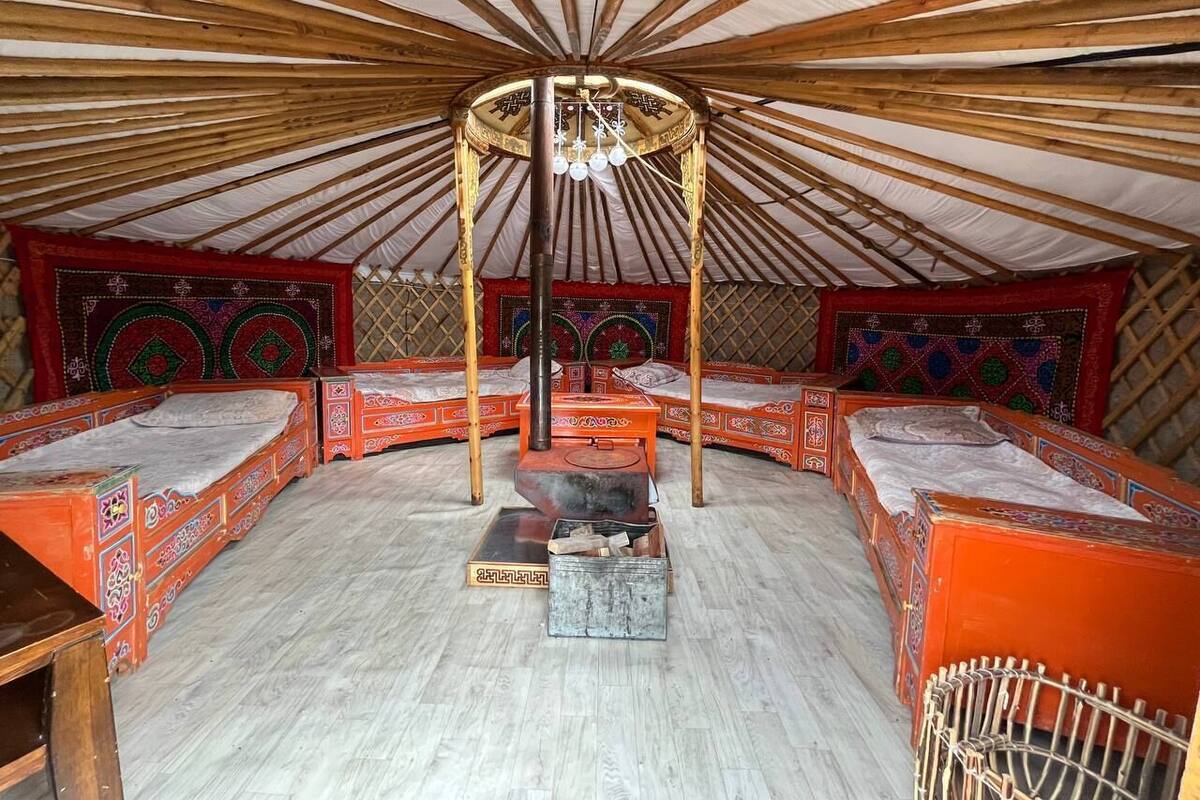 Interior tradicional de una yurtas con cuatro camas, un estufa de calefacción central y adornos decorativos en las paredes.
