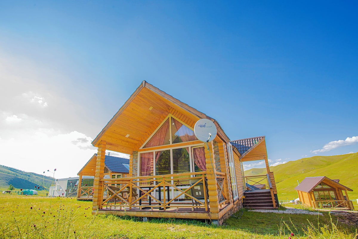 Una cabaña de madera con balcón, ventanas amplias y una antena parabólica.