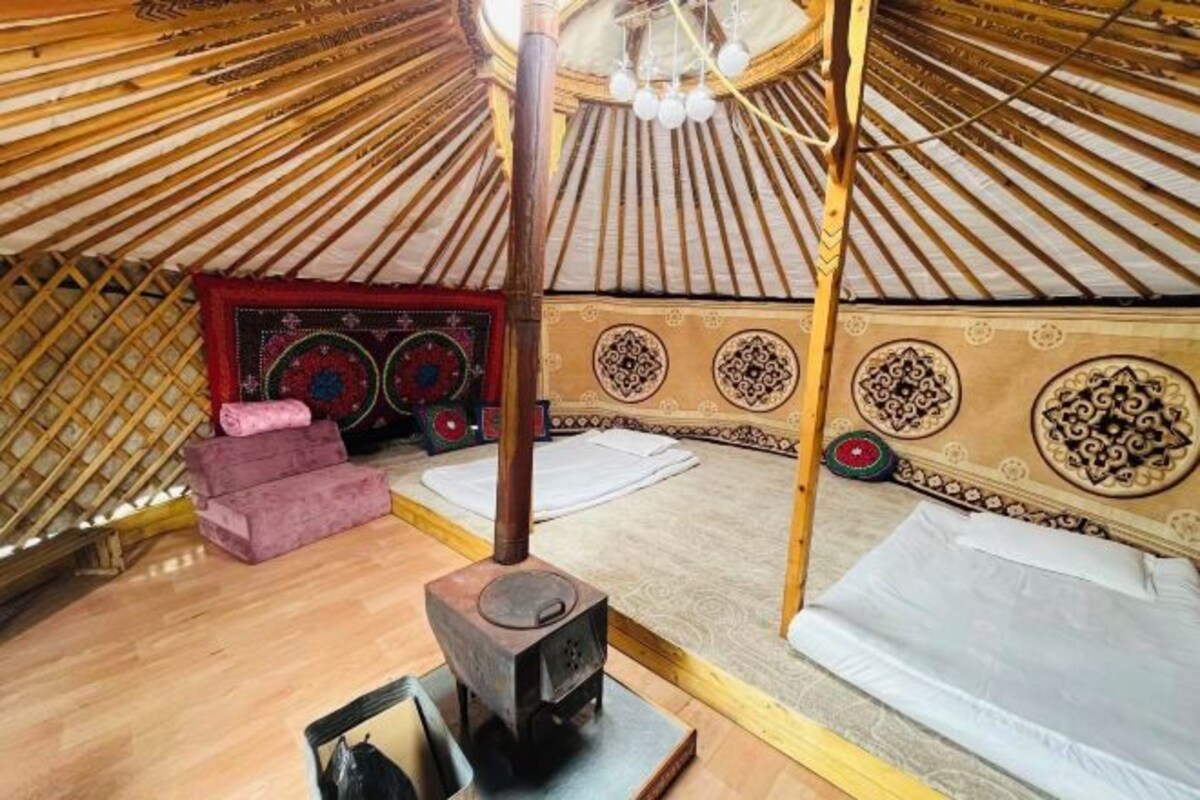 L’intérieur d’une yourte traditionnelle, avec un poêle central pour le chauffage, des sièges rembourrés et des motifs décoratifs sur les murs.