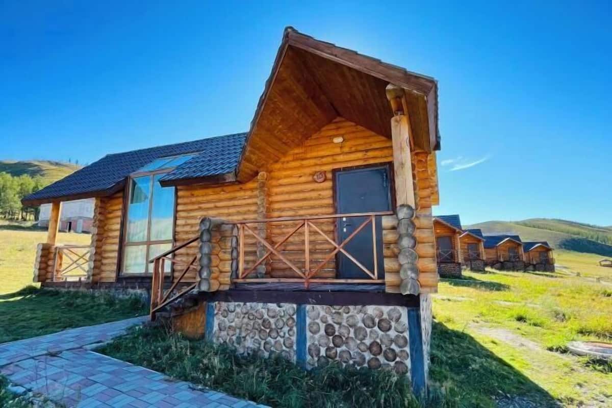 Una cabaña de madera con base de piedra, un porche y una vista despejada del paisaje circundante.