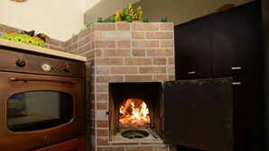 A brick fireplace with a fire, a wooden oven, and a black cabinet. - Villa with pool (Trappeto)