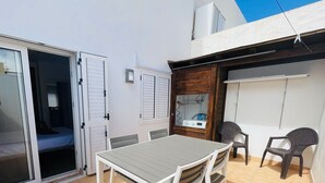 Une terrasse avec une table et des chaises, une porte-fenêtre coulissante et un petit espace clos équipé d’un radiateur.
