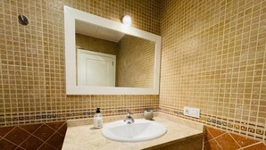 Une salle de bain avec un lavabo blanc, un miroir et un mur recouvert de carreaux.