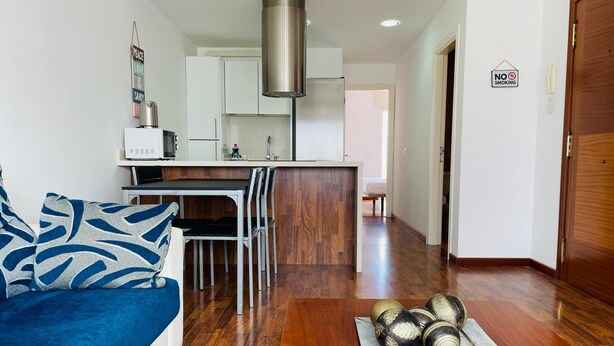 Un salon moderne avec un canapé bleu, une table basse en bois et un coin cuisine doté de meubles blancs et d’une hotte de cuisinière en acier inoxydable.