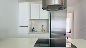 Une cuisine moderne avec des meubles blancs, une hotte en acier inoxydable et une plaque de cuisson à induction noire.