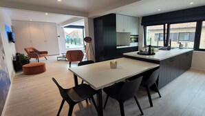 A modern kitchen with a dining area, featuring a large island, dark cabinetry, and a view of the outside. - Apartment in Zuienkerke with Terrace (zuienkerke)