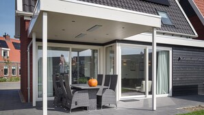 A covered outdoor patio with a table and chairs, a pumpkin, and a glass enclosure. - Holiday Home in Colijnsplaat (Colijnsplaat)