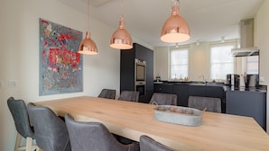 A modern kitchen with a central island, pendant lighting, and a dining area with a long table and chairs. - Holiday Home in Colijnsplaat (Colijnsplaat)