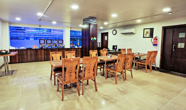 A restaurant with wooden furniture, a counter, and a blue wall with monitors. - RoseMallow Hotel New Delhi (New Delhi)