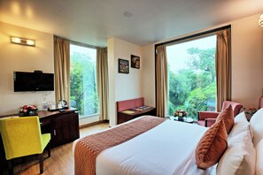 A hotel room with a bed, a desk, a chair, a television, and large windows with curtains. - RoseMallow Hotel New Delhi (New Delhi)