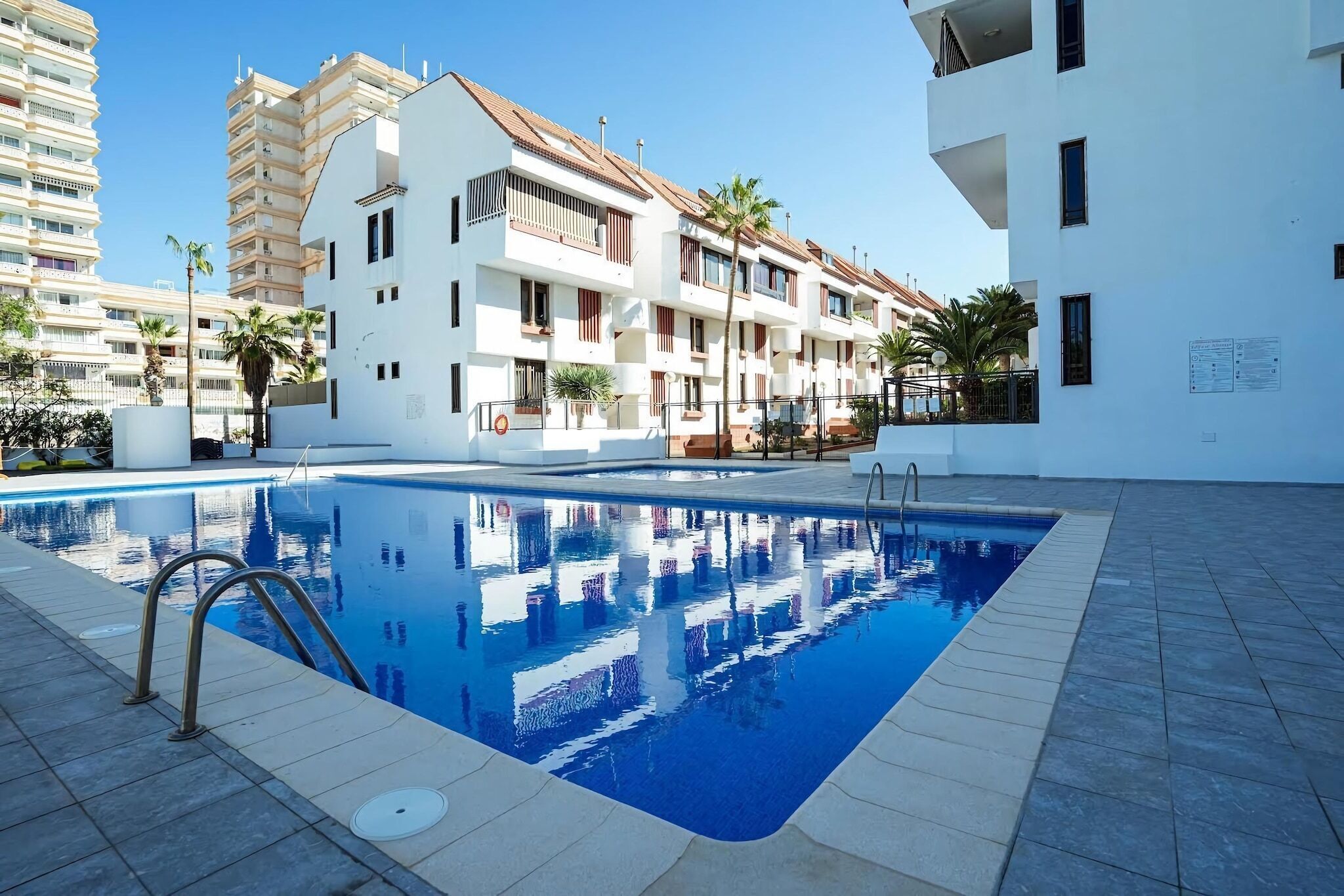 En swimmingpool med ett klart, blått vatten och en omgivande terrass som är belagd med plattor.