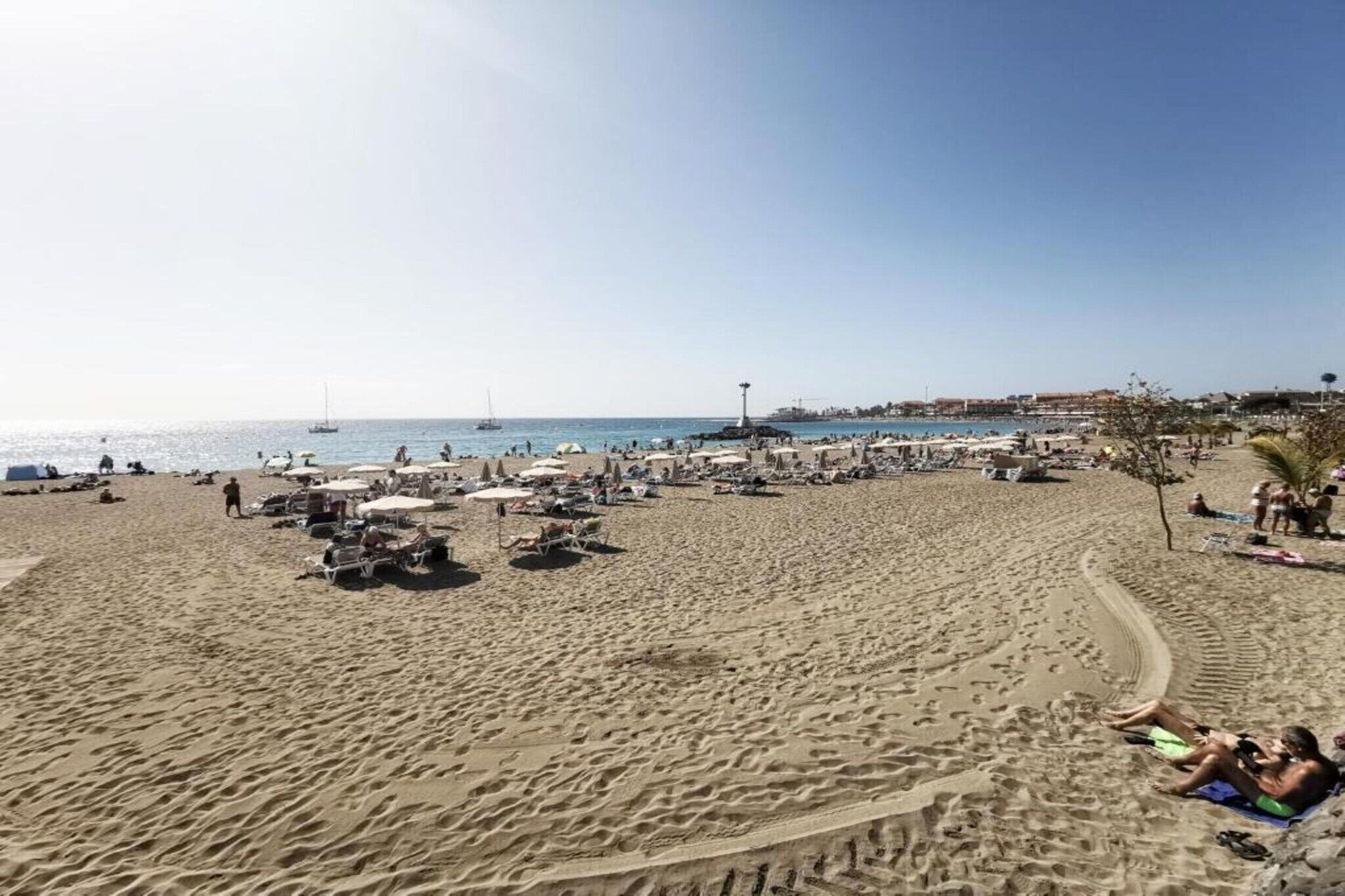 Ein Strand mit Liegestühlen, Sonnenschirmen und blauem Himmel.