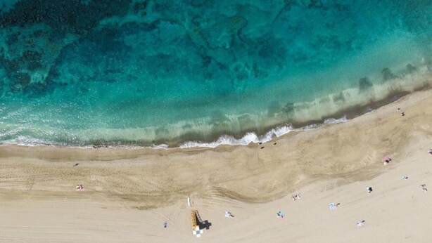 An aerial view of a beach with clear turquoise water, sandy shore, and people sunbathing. - Belvilla by OYO Apartment in Arona (Arona)
