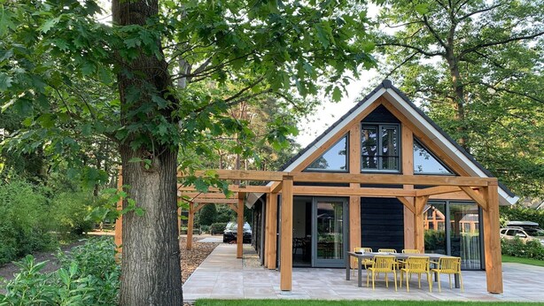 Una casa moderna con techo triangular, ventanas amplias y un patio con sillas amarillas.