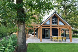 A modern house with a triangular roof, large windows, and a patio with yellow chairs.