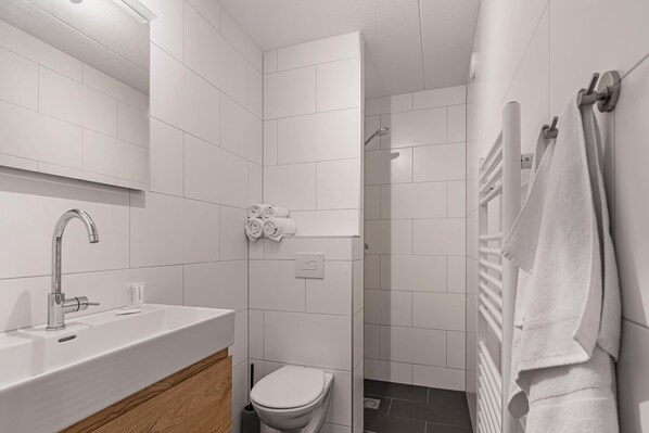 A modern bathroom with a white sink, toilet, and shower area.