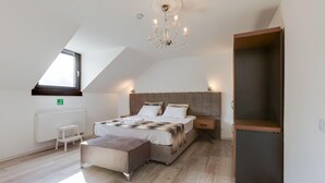 A bedroom with a sloped ceiling, a large bed, a nightstand, a bench, a radiator, and a window. - Apartment in Oberhausen near Lake & River (Oberhausen)