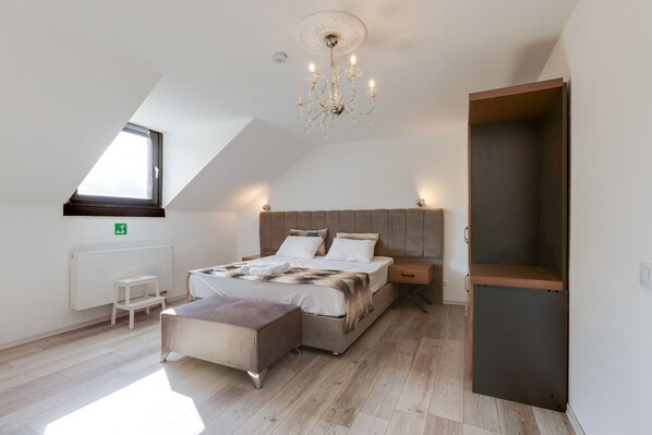 A bedroom with a sloped ceiling, a large bed, a nightstand, a bench, a radiator, and a window.
