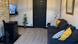 Una sala de estar con un sofá negro, televisión, chimenea y una puerta.