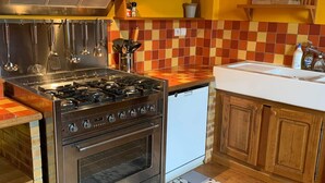 Cocina con estufa a gas, horno y utensilios colgantes. Se ve un lavamanos y un tapete estampado.