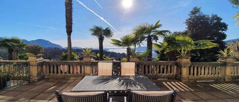 A patio with a table and chairs, surrounded by palm trees and a stone balustrade, overlooking a scenic landscape.