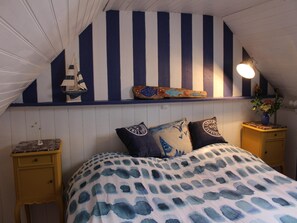 Een slaapkamer met een gestreepte wand, een bed met beddengoed met een patroon, twee nachtkastjes en een lamp.