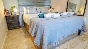 A bedroom with a wooden headboard, a large bed with white and blue bedding, a bedside table with a lamp, and a mirror on the wall. - Simba Apartment by Hello Homes Sitges (Sitges)