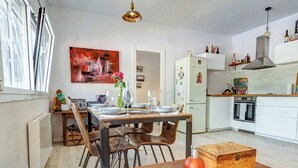 A dining area with a wooden table set for four, surrounded by chairs. A white refrigerator and oven are visible in the background. - Simba Apartment by Hello Homes Sitges (Sitges)