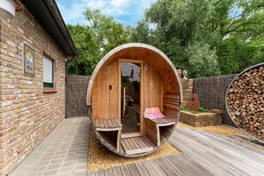 A wooden sauna structure with benches and a door, surrounded by a brick wall and wooden deck. - Restful Holiday Home in Koksijde with Hot Tub and Sauna (Oostduinkerke)