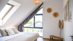 A bedroom with a sloped ceiling, a bed, a bench, and a large window. - Ein Strand- und Seehaus. 200m von der Camminer Bucht,1,8km vom Meer Entfernt (Zastań)