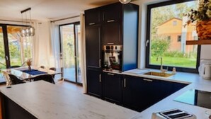 A modern kitchen with a large island, dark cabinetry, and a view of a house through the window. - Ein Strand- und Seehaus. 200m von der Camminer Bucht,1,8km vom Meer Entfernt (Zastań)