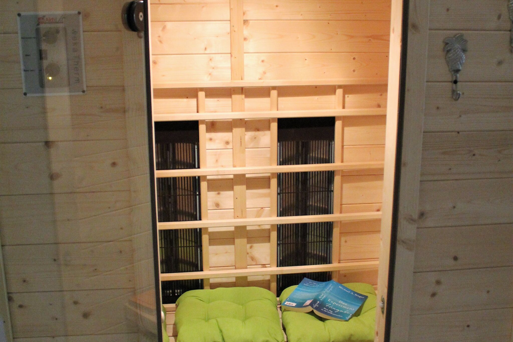 A wooden room with a green cushioned bench, a small table, and a wall-mounted thermostat.