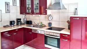 Uma cozinha moderna com armários vermelhos, exaustor de aço inoxidável, forno embutido, pia e máquina de café.