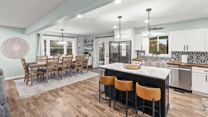 Una cocina moderna con una isla grande, taburetes de bar y un comedor con sillas de madera.