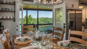 Comedor con una mesa dispuesta para cuatro, una araña y vistas a un lago.
