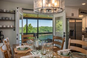 Un coin repas avec une table dressée pour quatre personnes, un lustre et une vue sur un lac.