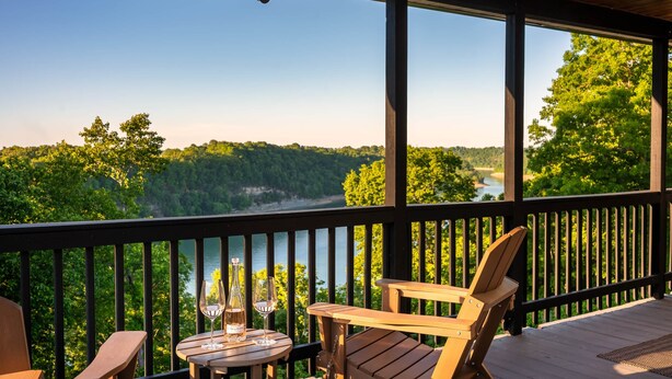 Una terraza de madera con una mesa y sillas, con vista a un lago y un bosque.
