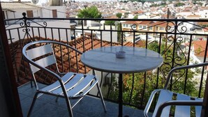 Ein Balkon mit zwei Stühlen und einem Tisch, mit Blick auf eine Stadtlandschaft mit roten Ziegeldächern und weißen Gebäuden.
