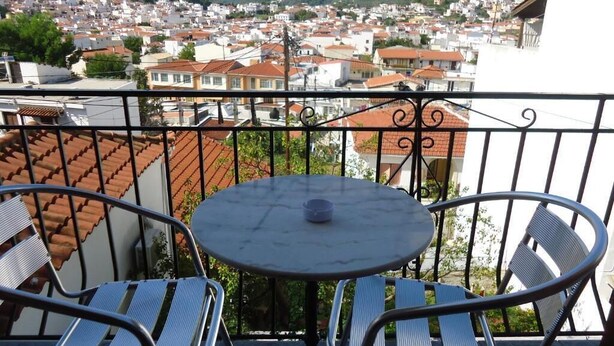 Ein Balkon mit rundem Tisch und zwei Stühlen, mit Blick auf ein Wohngebiet mit roten Ziegeldächern.