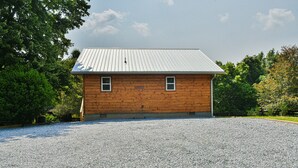 A wooden cabin with a metal roof, two windows, and a gravel driveway.