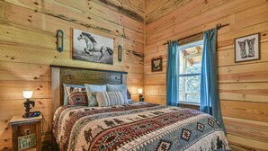A wooden cabin bedroom with a bed, a nightstand with a clock, and a window with curtains.