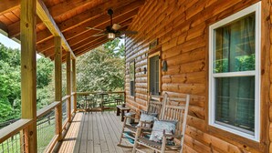 A wooden cabin with a porch, rocking chairs, and a view of the forest.