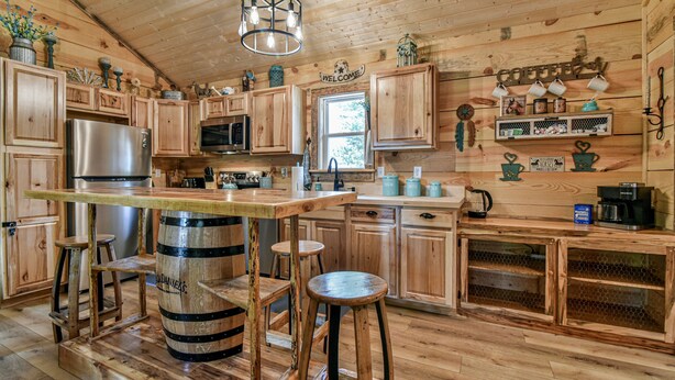 A rustic wooden kitchen with a bar area, wooden stools, and a large barrel as a central feature.